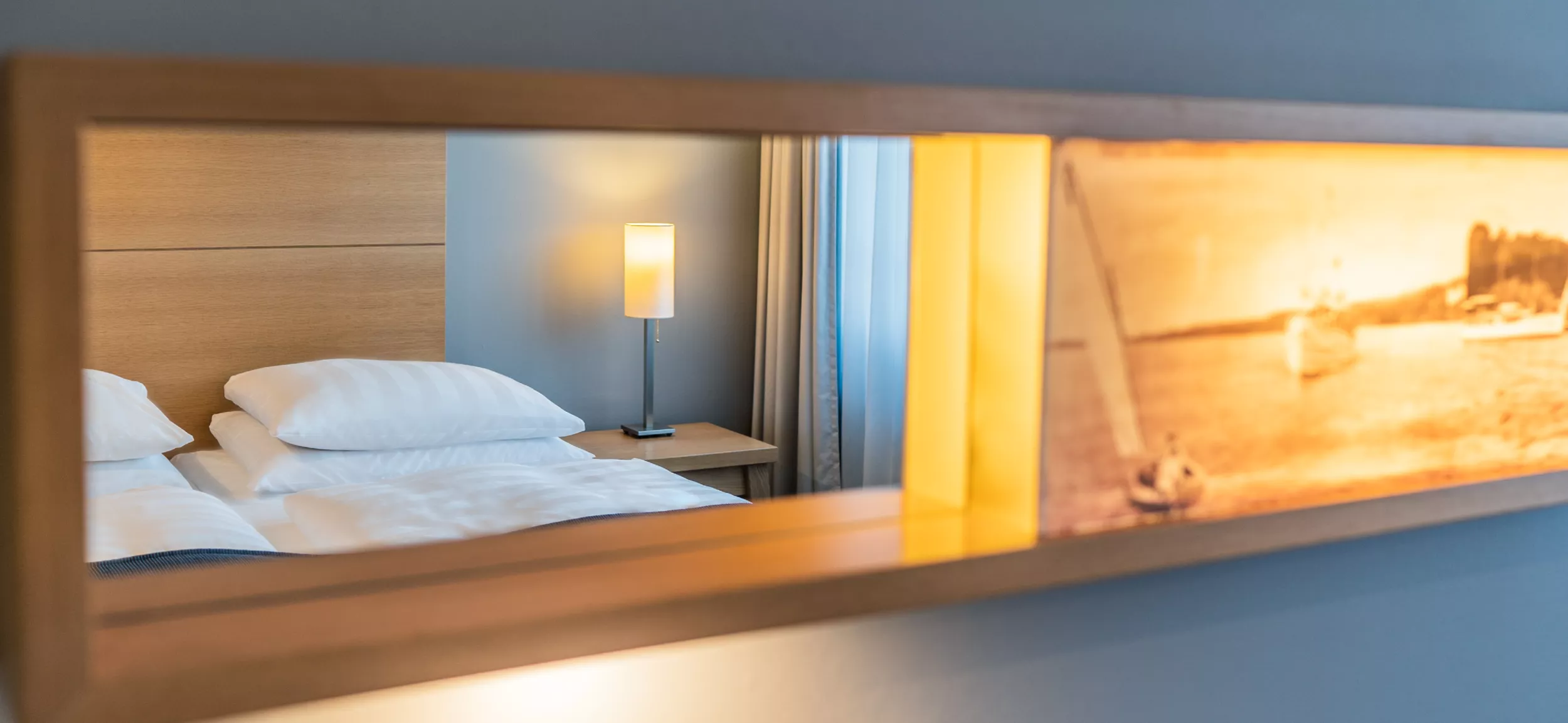 Spiegel fotografiert, darin spiegelt sich Kopfende von Doppelbett mit Nachttischlampe