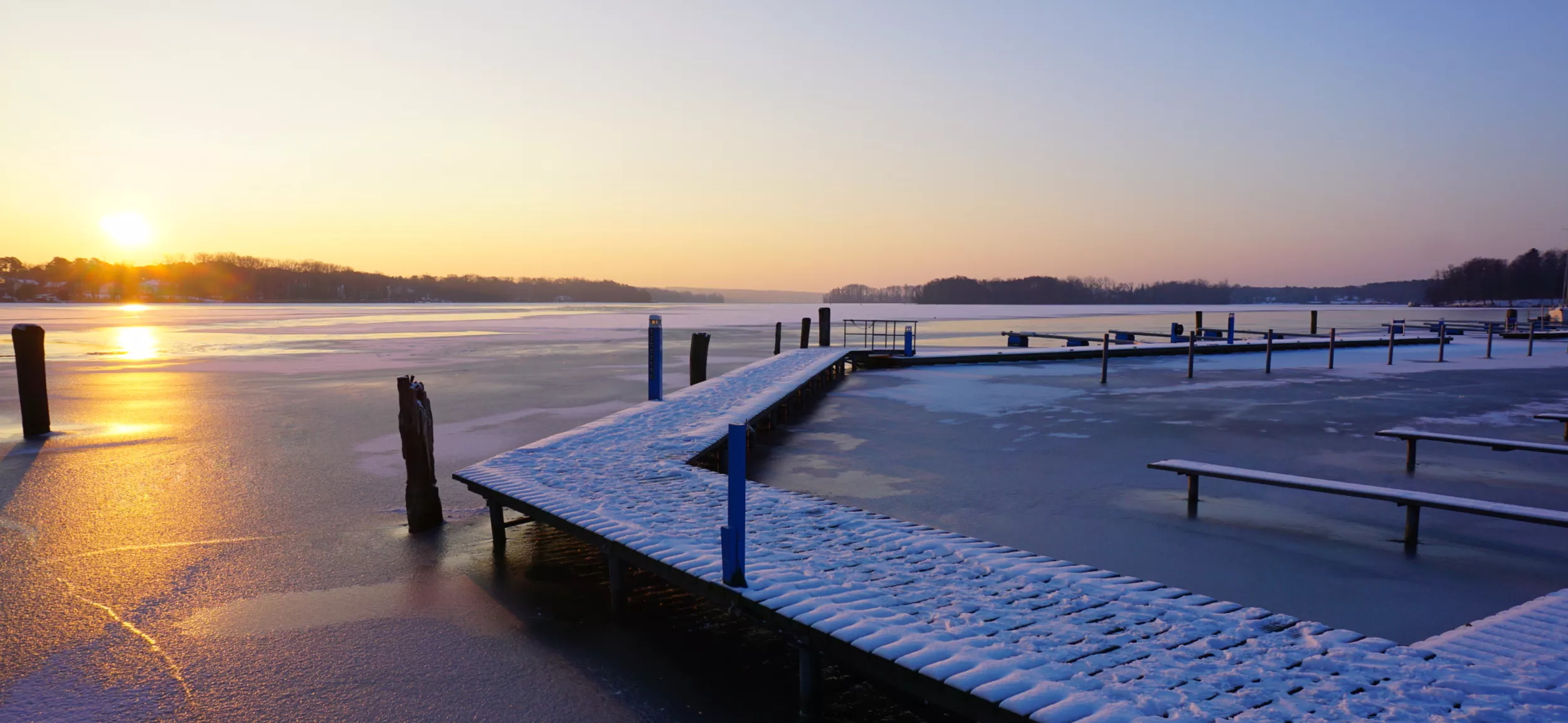 zugefrorener See mit Schnee auf Steg, bei Sonnenaufgang