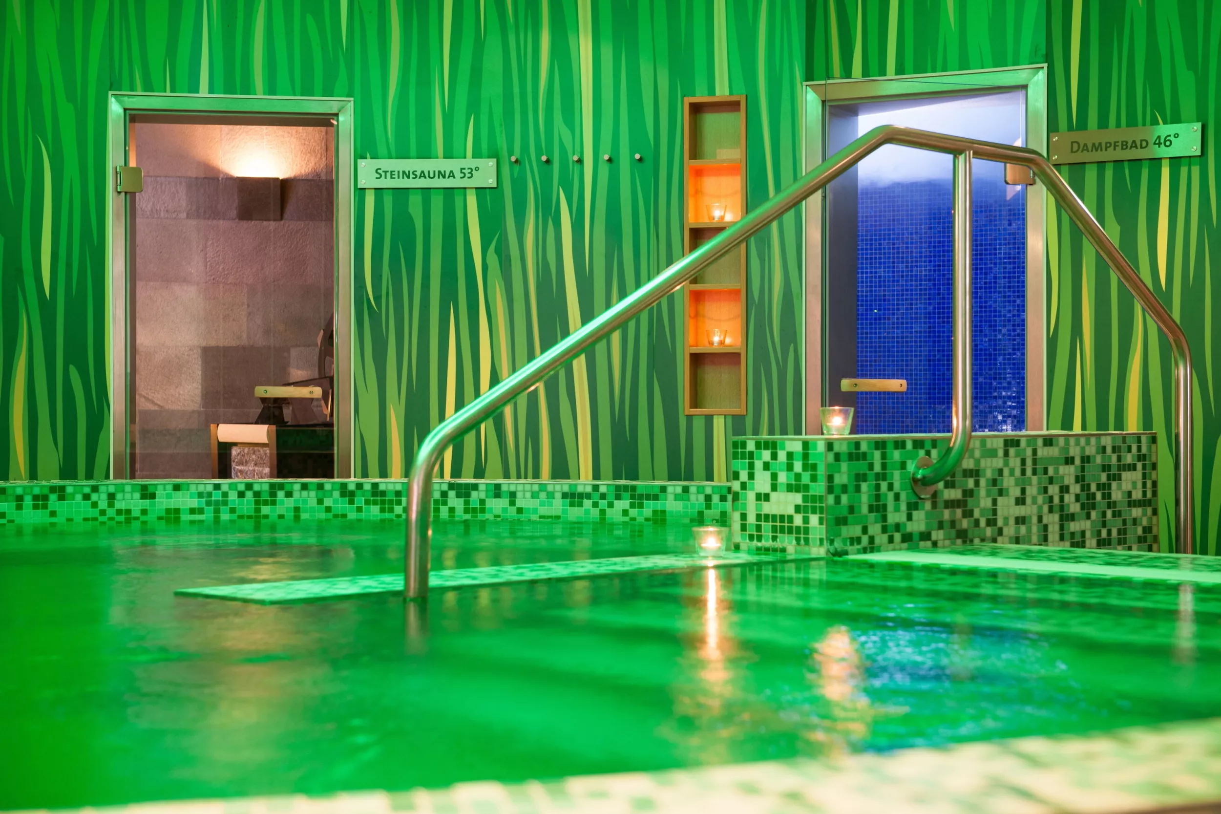 Pool mit grüner Wand und grünem Licht, hinten Türen zur Sauna
